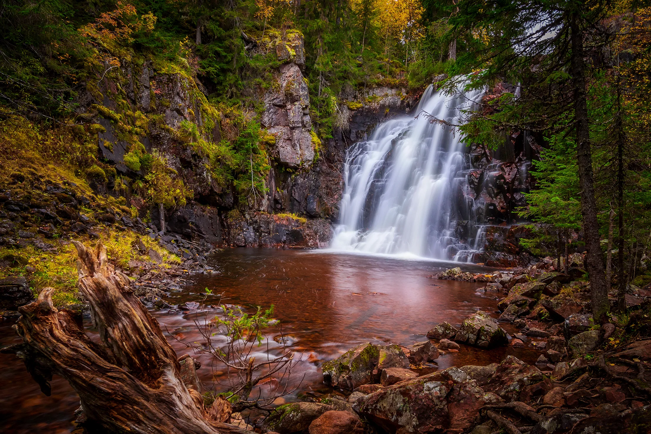 Stopfallet med vattenfall som rinner ner i bassäng omgiven av skog och klippor.