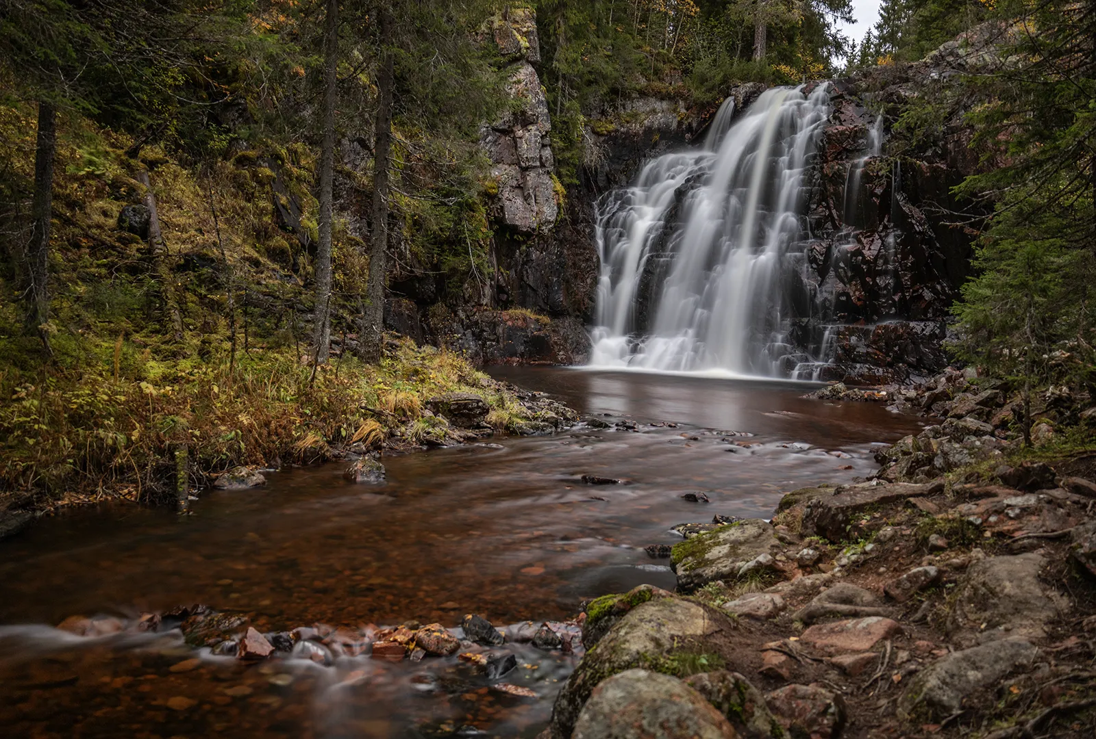 Stopfallet fotograferat i vidvinkel med vattenfallet som rinner ner i en stilla bassäng i skogen.